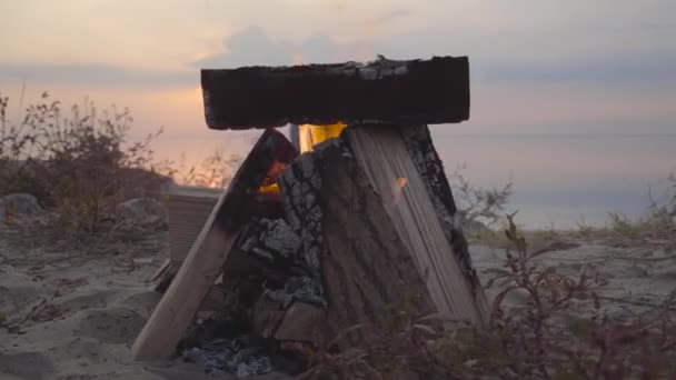 Hoguera naranja ardiente hecha de maderas en el fondo de impresionante puesta de sol de colores cerca de la orilla del mar y besar a la pareja. De cerca. — Vídeos de Stock