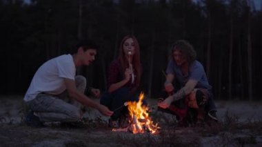 Üç genç arkadaş sahilde bir yangın ile marshmallow salma ve rahat yaz akşamı sohbet ürpertici