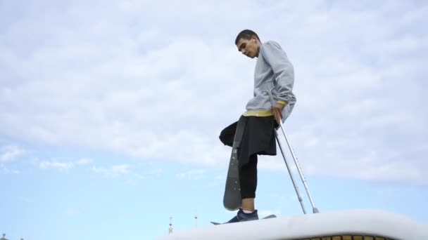 Junger Mann mit einem Bein auf Krücken beim Skateboardtraining. Behinderte fahren auf einem Skateboard. der Typ nach einem Trauma, der sein Leben neu erschafft und genießt. Motivation, aktiver Lebensstil, niemals aufgeben — Stockvideo