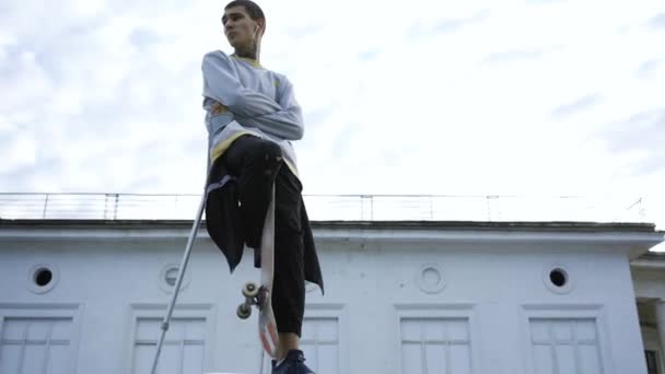 Handsome young man with one leg on crutches training with skateboard. Disabled person rides on a skateboard. The guy after trauma recreating and enjoying his life. Motivation, active lifestyle, never — Stock Video
