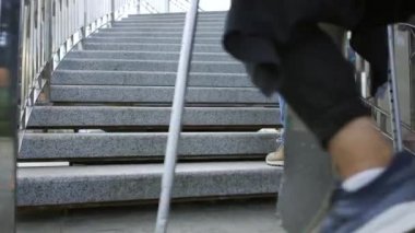 Tek bacağı koltuk değnekleriyle kaykaylı genç adam merdivenlerden arkadaşından daha hızlı tırmanıyor. Engelli kişinin aktif yaşamı. Bacağı olmayan adam hayatından zevk alıyor. Motivasyon, asla vazgeçme