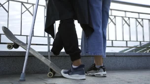Okänd man med ett ben på kryckor med skateboard pratar med sin flickvän på gatan. Aktivt liv för personer med funktionshinder. Killen utan ben njuter av sitt liv. Motivation, ge aldrig upp. — Stockvideo
