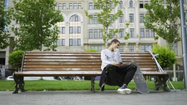 Parkta bankta oturan genç adam cep telefonundan müzik dinliyordu. Koltuk değnekleri ve kaykay yakınlardadır. Engelli kişinin aktif yaşamı. Motivasyon, normal hayat, asla vazgeçme
