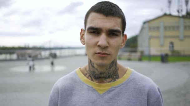 Portrét mladého muže s tetováním na krku, který stál proti obloze s mraky. Chlápek, co se dívá na kameru. — Stock video