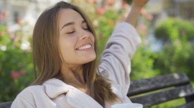 Sevimli sevinç portre kahve veya çay içme parkta bankta oturan genç kadın gülümseyen. Kendine güvenen kız güzel sabah açık havada zevk. Kaygısız yaşam
