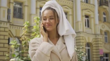 Sokakta cep telefonu ile konuşurken baş havlu ile bornoz sevimli gülümseyen jou genç kadın Portresi. Kendinden emin kız şehirde güzel bir gün zevk