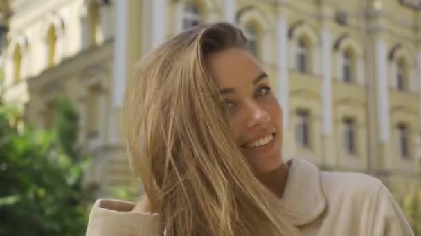 Porträtt av leende ung kvinna skicka luft kyss tittar på kamera leende stående på gatan. Självsäker tjej njuter av en vacker dag utomhus. — Stockvideo