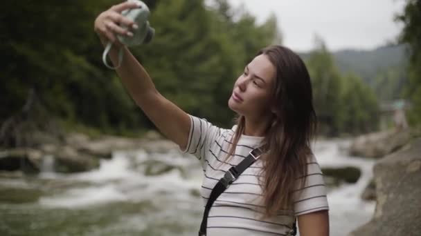 Mulher bonita tomando selfie de pé em frente ao rio da montanha. Conexão com a natureza selvagem. Lazer ao ar livre, estilo de vida ativo . — Vídeo de Stock