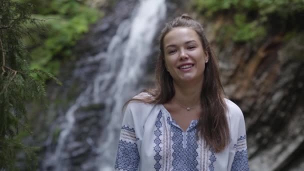 Ritratto di giovane donna con lentiggini sul viso che guarda la macchina fotografica di fronte alla cascata. La ragazza che passa del tempo all'aperto. Connessione con la natura. Rallentatore — Video Stock