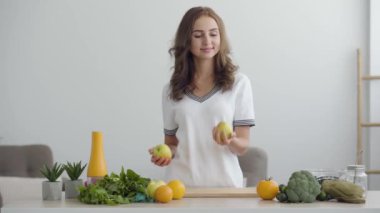 Genç gülümseyen kadın kusuyor ve modern mutfakta masada duran elma yakalar. Sağlıklı gıda kavramı. Nutri terapisti, nutraceutical, beslenme uzmanı, sağlıklı yaşam koçu mesleği