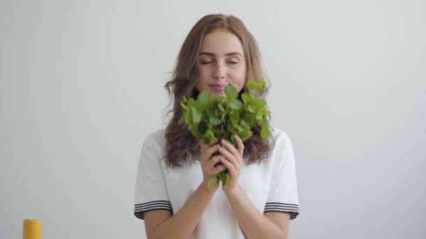 Mujer bonita joven olfateando verduras frescas de pie en la mesa en la cocina moderna. Concepto de comida saludable. Profesión de nutri terapeuta, nutracéutico, nutricionista, entrenador de bienestar — Vídeo de stock