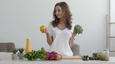 Genç gülümseyen kadın modern mutfakta masada duran sarı domates ve brokoli tutan. Sağlıklı gıda kavramı. Nutri terapisti, nutraceutical, beslenme uzmanı, sağlıklı yaşam koçu mesleği