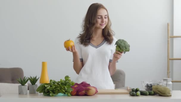 Porträtt ung kvinna som innehar gul tomat och broccoli stående vid bordet i modernt kök. Begreppet hälsosam mat. Yrke Nutri terapeut, nutraceutical, nutritionist, Wellness coach — Stockvideo