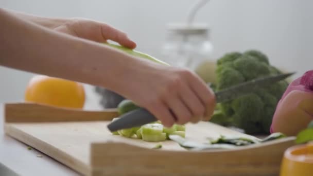 Primer plano de las manos femeninas rebanando verduras con el cuchillo afilado en la cocina. Concepto de comida saludable. Frutas y verduras tumbadas sobre la mesa — Vídeos de Stock