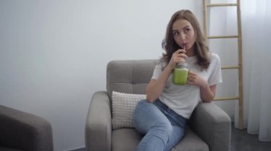 Güzel genç kadın evde mutfakta küçük kavanozdan lezzetli smoothie içme. Sağlıklı gıda kavramı. Nutri terapist, beslenme uzmanı, sağlıklı yaşam koçu mesleği. Kamera yaklaşıyor