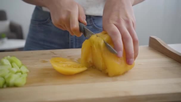女手在厨房的桌子上用锋利的刀切开大黄番茄的特写镜头。健康食品的概念。营养师、营养学家、营养师的职业. — 图库视频影像