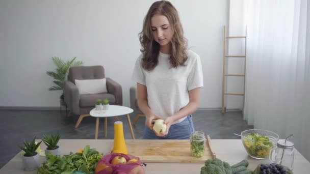 Hermosa joven mujer delgada pelando manzana con el cuchillo afilado de pie en la mesa en la cocina. Concepto de comida saludable. Profesión de nutri terapeuta, nutracéutico, nutricionista — Vídeos de Stock