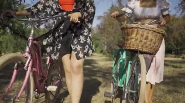 Dışarıda yürüyen iki güzel genç kadın. Sokaktaki dar yolda bisikletlerini süren kızlar konuşuyor. Kırsal yaşam. Retro tarzı. Güzel yaz günü.