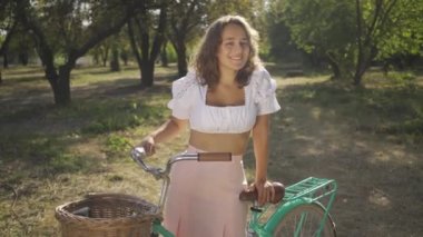 Bisikleti ile bahçede veya parkta duran kıvırcık saçlı çekici genç kadının portresi. Kırsal yaşam. Retro tarzı. Güzel yaz günü zevk Ülke kız