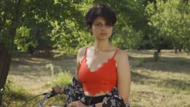 Kısa siyah saçlı güzel genç kadının portresi bahçede ya da parkta kameraya bakarak bisikletiyle duruyor. Kırsal yaşam. Retro tarzı. Güzel yaz günü zevk Ülke kız