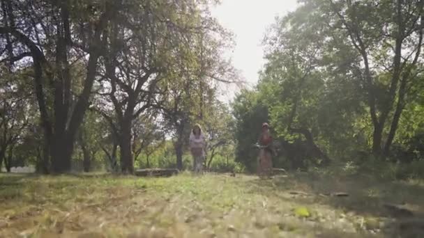 Dos mujeres jóvenes montando bicicletas en el parque o jardín de verano. Chicas pasando por la cámara. La vida rural. Estilo retro. Hermoso día de verano — Vídeo de stock