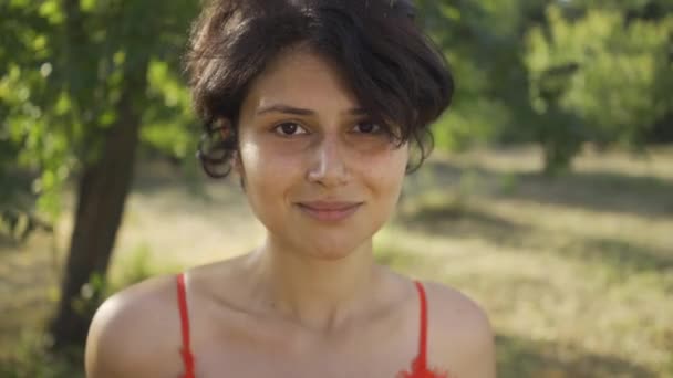 Retrato de una linda joven con el pelo negro corto de pie en el jardín o el parque con su bicicleta mirando a la cámara. La vida rural. Estilo retro. Chica del campo disfrutando de hermoso día de verano — Vídeo de stock