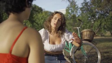 Yaz bahçesinde birlikte otururken konuşan iki genç kadın, bisikletlerinin yanında duruyor. Kırsal yaşam. Retro tarzı. Güzel bir yaz günü. Omzundan ateş etme