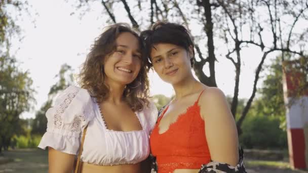 Güneş ışınlarının önünde gülümseyen kameraya bakan iki güzel kadının portresi. Güzel lezbiyen çift gün batımının tadını çıkarıyor. Romantik tarih, aşk, ihale ilişkisi — Stok video