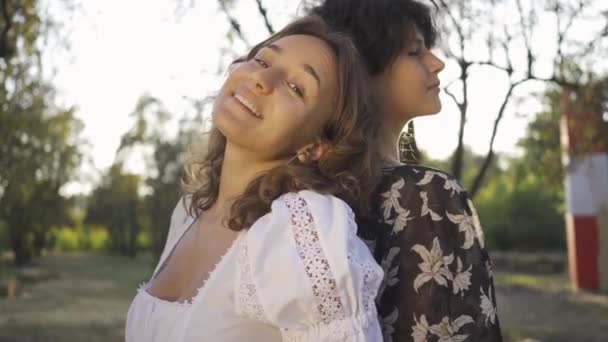 Retrato de dos mujeres lindas paradas espalda con espalda mirando a la cámara sonriendo. Hermosa pareja lesbiana disfrutando estar juntos. Cita romántica, amor, tierna relación — Vídeos de Stock