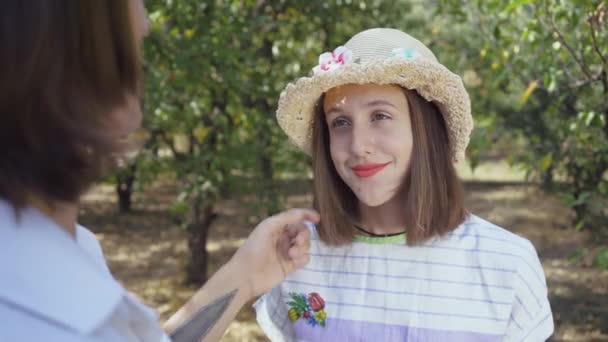 Linda pareja de pie bajo los árboles en el parque, el hombre con el pelo largo tocando el pelo de la mujer bonita en el sombrero. Los amantes pasan tiempo juntos al aire libre. Estilo retro. Disparos sobre el hombro — Vídeo de stock