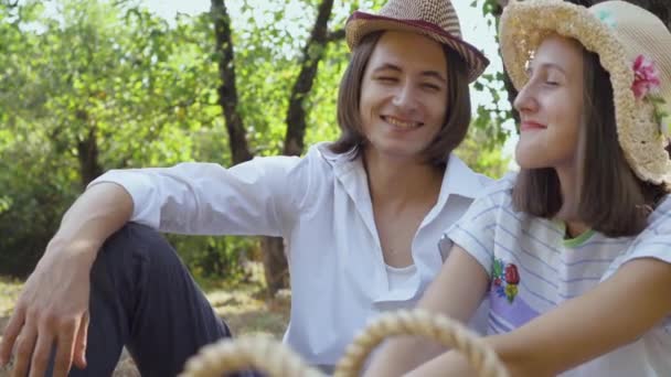 Милая кавказская пара, сидящая в парке, улыбающаяся и разговаривающая. Мужчина с длинными волосами и симпатичная женщина в шляпе проводят время вместе на улице. Ретро стиль . — стоковое видео