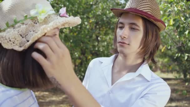 Linda pareja de sombreros de pie en el parque, el hombre con el pelo largo tocando el pelo de la mujer bonita en el sombrero. Los amantes pasan tiempo juntos al aire libre. Estilo retro. Disparos sobre el hombro . — Vídeos de Stock