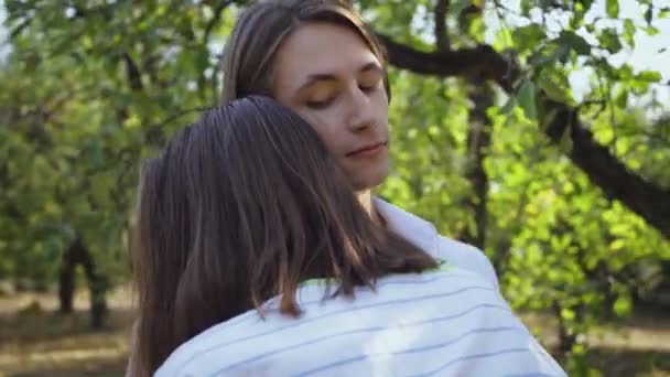 Feliz pareja joven abrazándose y sonriendo felizmente mientras está de pie en el parque o el jardín. Ocio al aire libre, conectando con la naturaleza. Cámara moviéndose . — Vídeo de stock