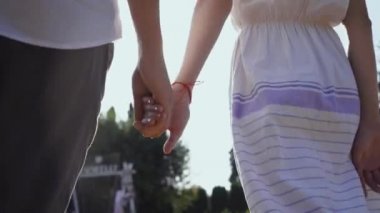 Parkta ya da bahçede el ele yürüyen çift. Erkek ve kadın dışarıda birlikte vakit geçiriyorlar. Geri görünüm.