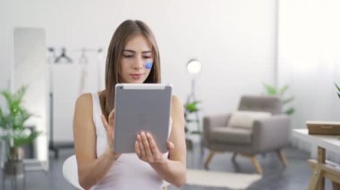 Yüzünde mavi boyalı sosyal medya simgesi ile genç çekici kadın portresi tabletine bakarak ve gülümseyerek. Gadget'lara bağımlılık.