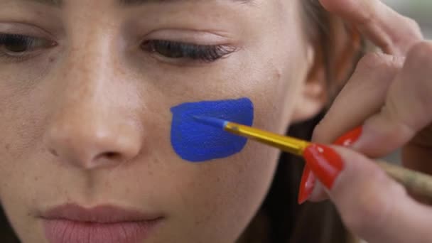 Genç ve güzel bir kadının yüzü. Sanatçı boyama mavi simgesi kızlar üzerinde küçük yumuşak fırça kullanarak yüz. Vücut sanatı konsepti. Bir insan vücudunda küçük sanat — Stok video