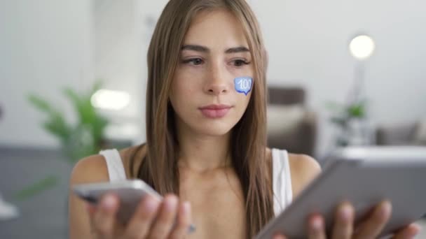 Retrato de una mujer joven y atractiva con una caja de mensajes pintada en la cara sosteniendo el teléfono y la tableta en las manos y sonriendo mirando a la cámara. Concepto de redes sociales. Adicción a los aparatos — Vídeos de Stock