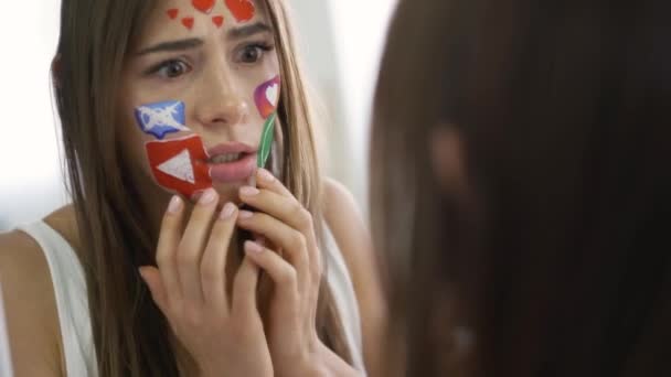 Retrato de una joven hermosa mujer con iconos pintados en las redes sociales en su cara mirándose en el espejo con horror. Adicción a gadgets, problemas, comunicación web . — Vídeos de Stock