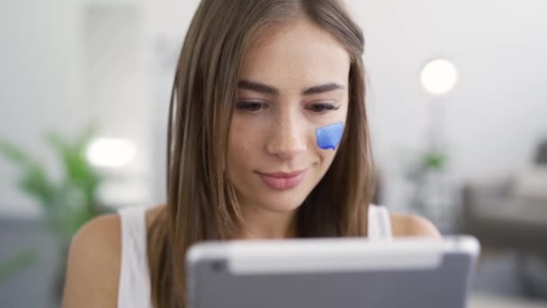 Gros plan portrait de jeune femme mignonne obtenir de bonnes nouvelles de sa tablette assis à la maison. Boîte aux messages peinte sur le visage des filles. Concept de médias sociaux. Dépendance au gadget. Tomber amoureux d'un en ligne — Video