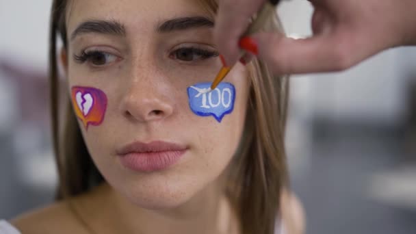 Primer plano de la joven mujer caucásica con iconos pintados en las redes sociales en su cara mirando a la cámara. Adicción a gadgets, comunicación web. Concepto de redes sociales . — Vídeo de stock