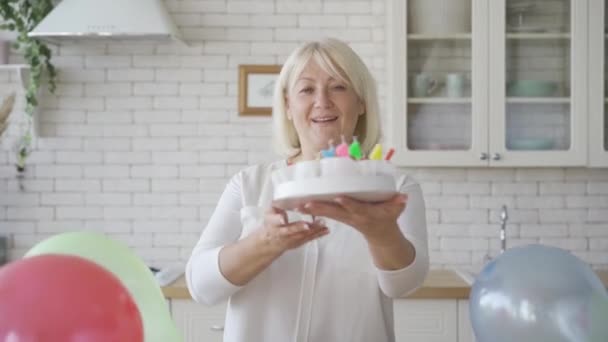 Eine Seniorin zeigt eine Torte, die für ihr Kind oder Enkelkind zubereitet wurde. Geburtstagsfeier. Fürsorgliche Oma bereitet Geschenk vor. — Stockvideo