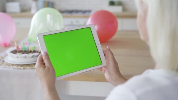 Handen van rijpe vrouw het houden van witte tablet met groen scherm. Verjaardag viering. Chromakey. Schieten over de schouder — Stockvideo