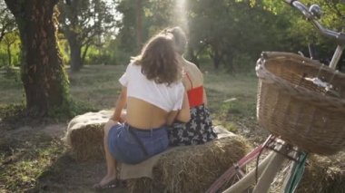 Yaz bahçesinde birlikte oturan iki sevimli kadın arka görünümü, onların bisiklet yanında duran. Güzel lezbiyen çift. Kırsal yaşam. Retro tarzı. Sıcak yaz günü