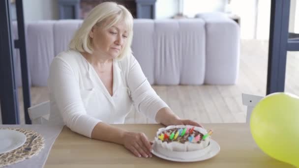 Triste femme mûre malheureuse assise à la table devant un petit gâteau d'anniversaire dans une pièce emlpy puis se lève et s'en va. Concept de célébration d'anniversaire. Tristesse, solitude — Video