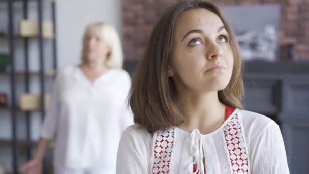 Porträt einer jungen Frau im Vordergrund, die sich mit ihrer Mutter streitet. Seniorin gestikuliert emotional im Hintergrund und streitet mit ihrer Tochter. schwierige familiäre Beziehung. — Stockvideo