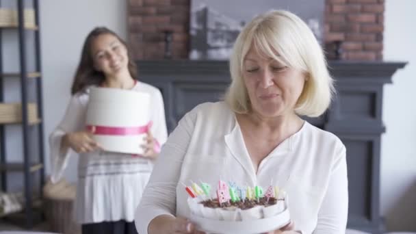 Mujer mayor mostrando un pastel a la cámara. Mujer joven de pie con el presente en el fondo Concepto de celebración de cumpleaños . — Vídeo de stock