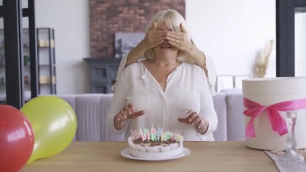 Η κόρη έκανε πάρτι γενεθλίων για τη μητέρα της. Μια νεαρή γυναίκα που κάλυπτε τα μάτια της μάνας της πριν δείξει την τούρτα και την παρουσία της. Γιορτή γενεθλίων. Έκπληξη — Αρχείο Βίντεο