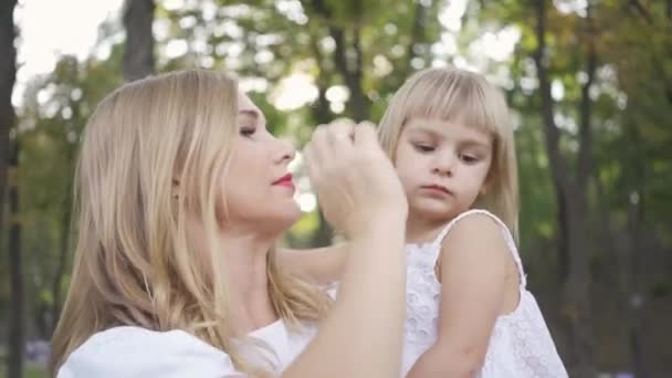 Porträt einer jungen blonden Frau im weißen Kleid, die ihre süße Tochter streichelt. Freizeit im Freien. glückliche Familie. ein Elternteil. Mutterschaft, Elternschaft, glückliche Kindheit — Stockvideo