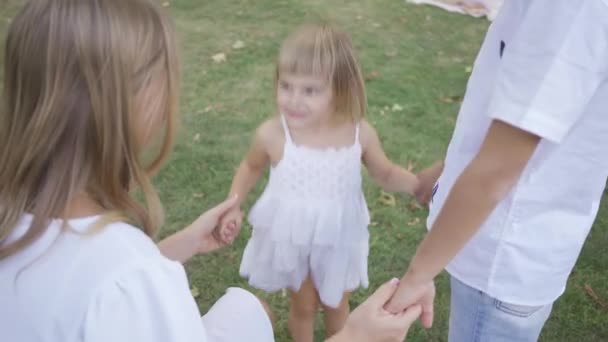 Happy little girl jumping up while holding parents hands in the park. A child spending time with family. Childhood, parenthood, good relations. — Stock Video