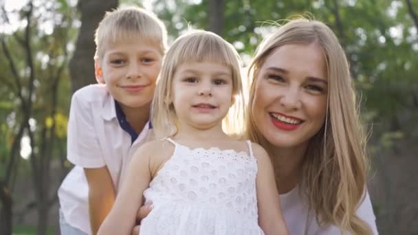 Mulher loira bonita e seus dois filhos olhando para a câmera sorrindo. Menino, menina e mulher atraente se divertir no parque. Retrato de família feliz com dois filhos — Vídeo de Stock